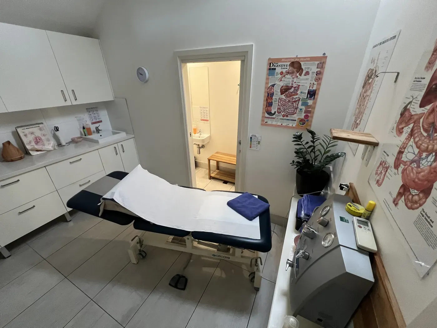 A colonic irrigation room with the closed-system machine beside the treatment table and a door through to the ensuite