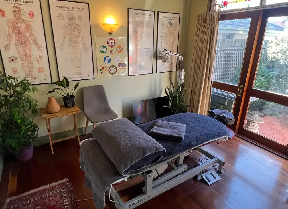 A massage and acupuncture room with a treatment table and meridian charts on the wall