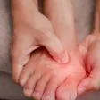 Hands cradling a foot, with the joint at the base of the big toe highlighted in red
