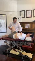 A chiropractor moving a patient's bent leg while they lie on a treatment table