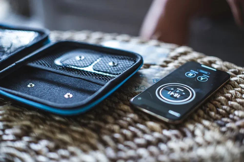 The pods and their carry case on a woven mat, next to a phone running a program