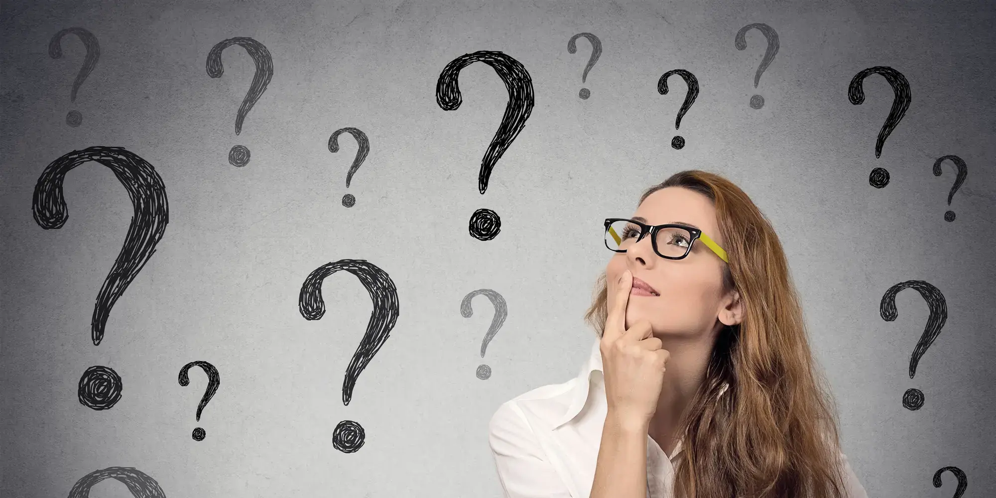 A woman looking up in thought, surrounded by hand-drawn question marks on a wall