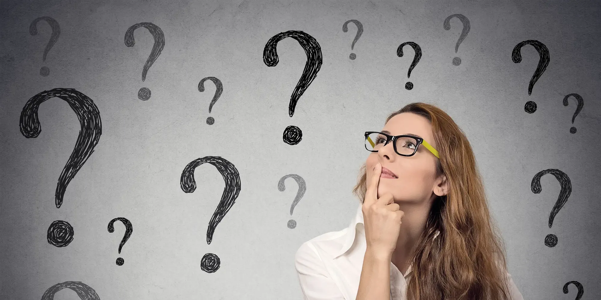 A woman looking up in thought, surrounded by hand-drawn question marks on a wall