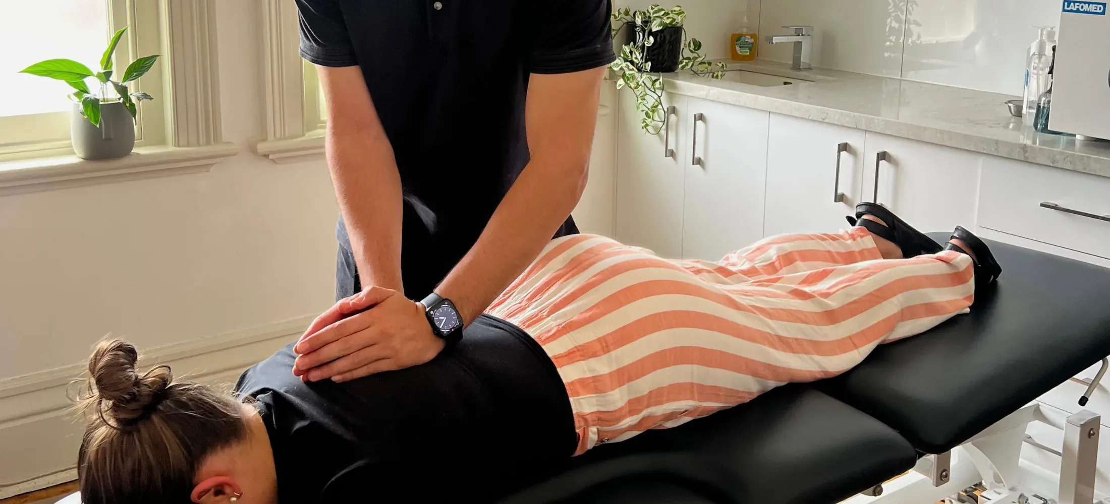 A practitioner with both hands on a patient's mid-back as the patient lies face down on a treatment table