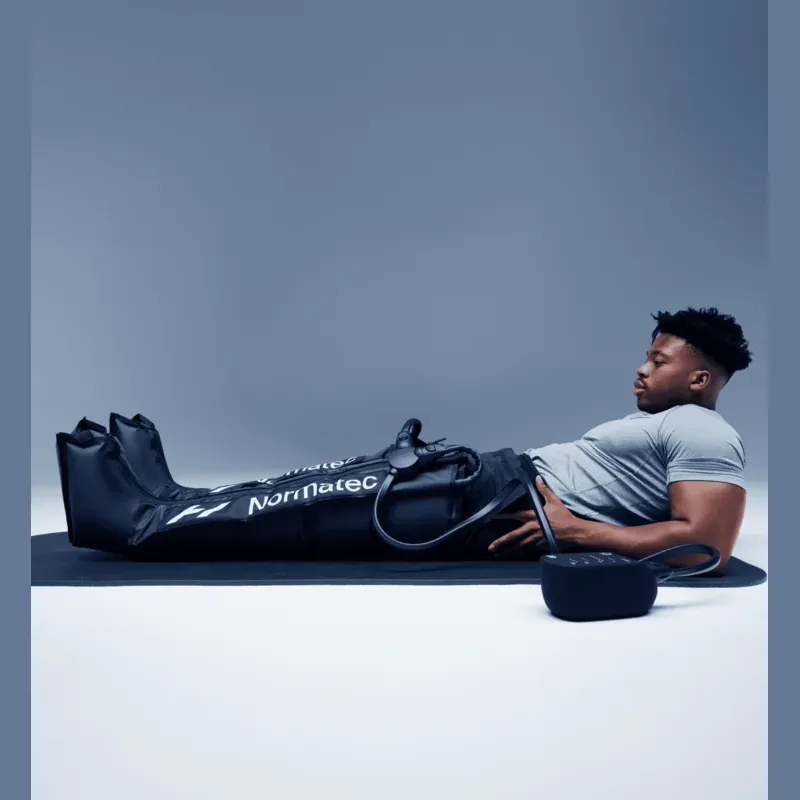 A man lying back with both leg attachments zipped on, the control unit beside him
