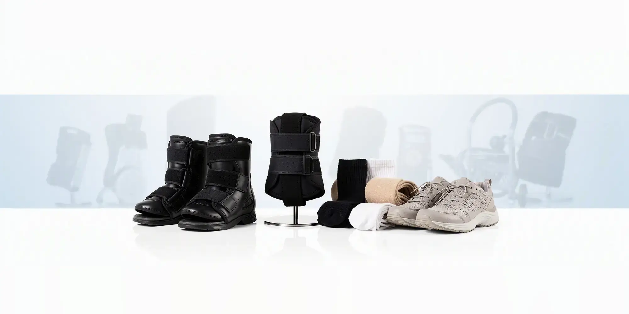 Moon boots, a back brace, compression socks and stockings and a pair of medical walking shoes, lined up on a pale studio background