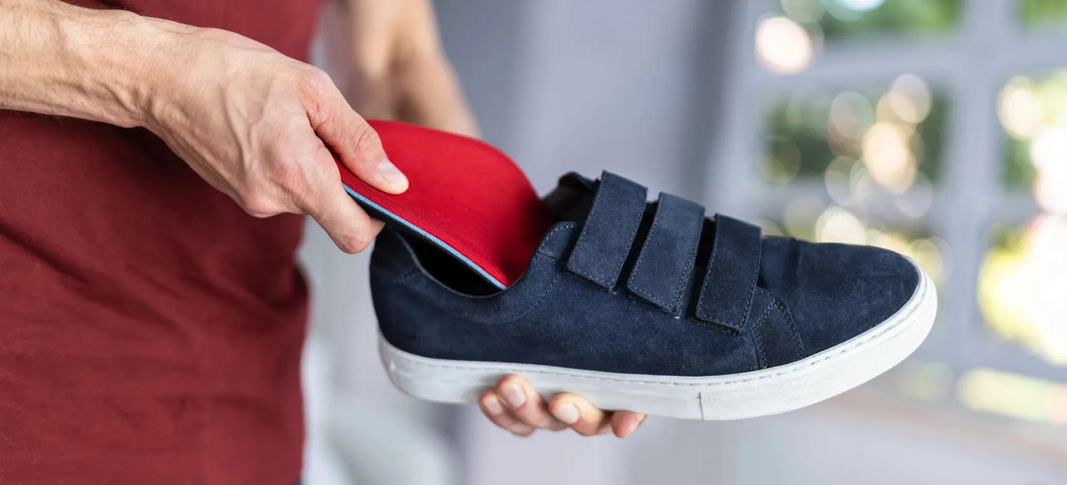 Hands fitting a red orthotic insole into a navy shoe