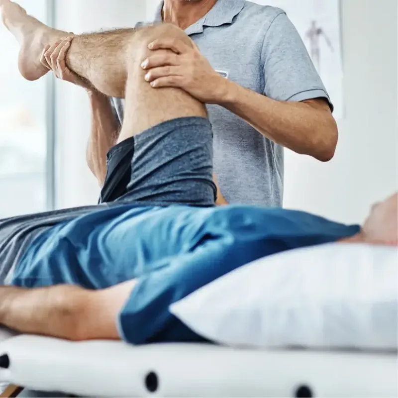 A physiotherapist assessing a patient's knee on a treatment table