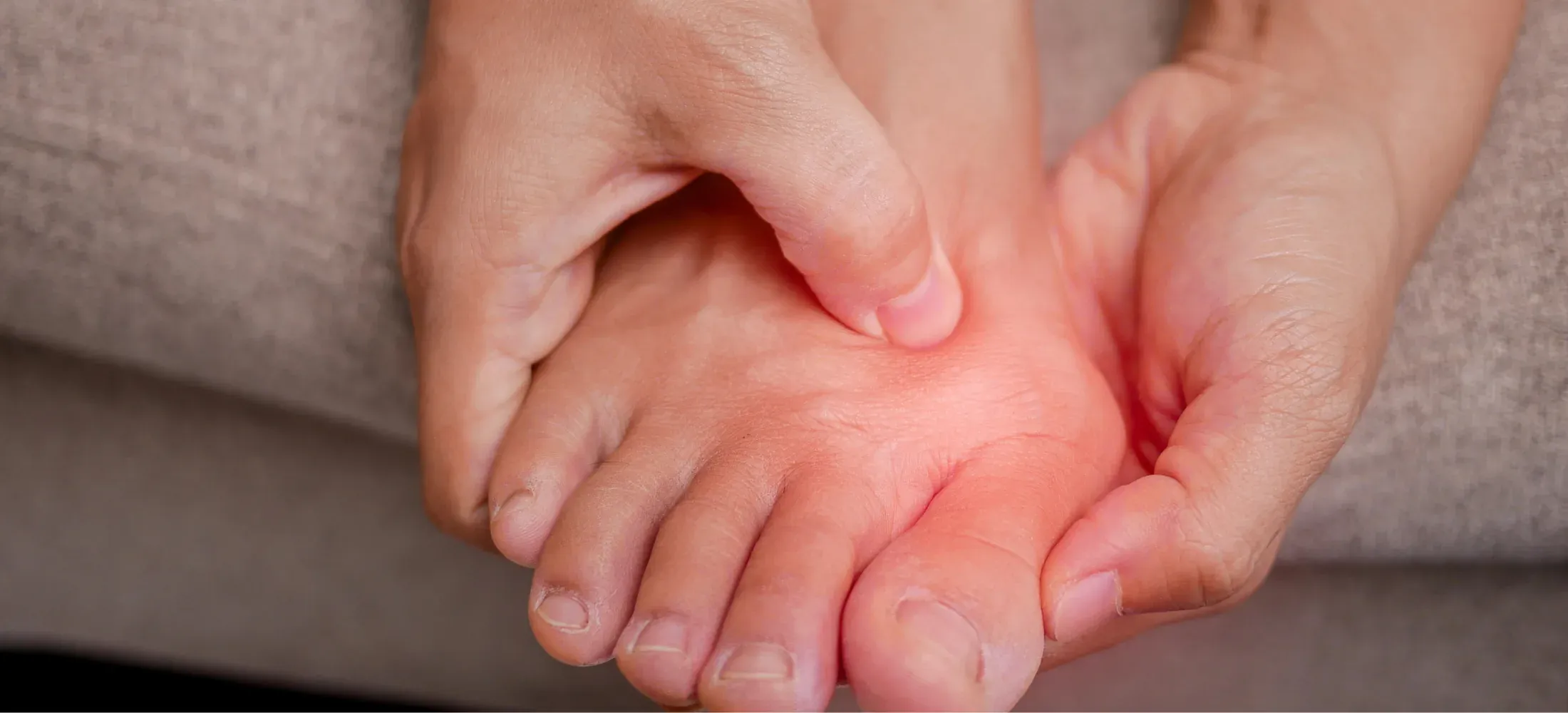 Hands holding a bare foot, the joint at the base of the big toe reddened