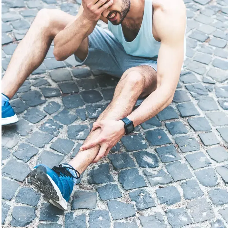 A runner sitting on pavement holding their shin