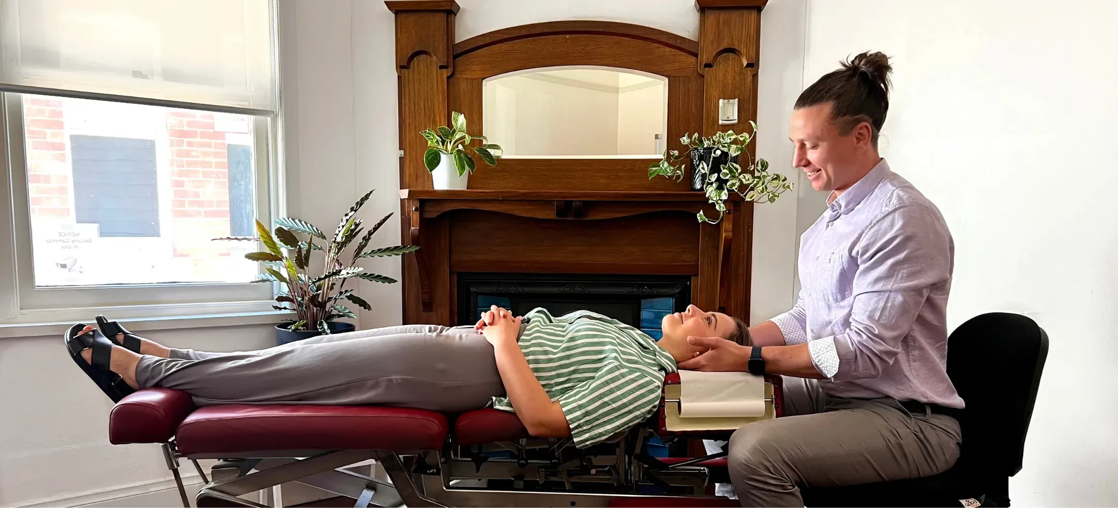 A practitioner supporting a patient's neck on a treatment table in the clinic's front room