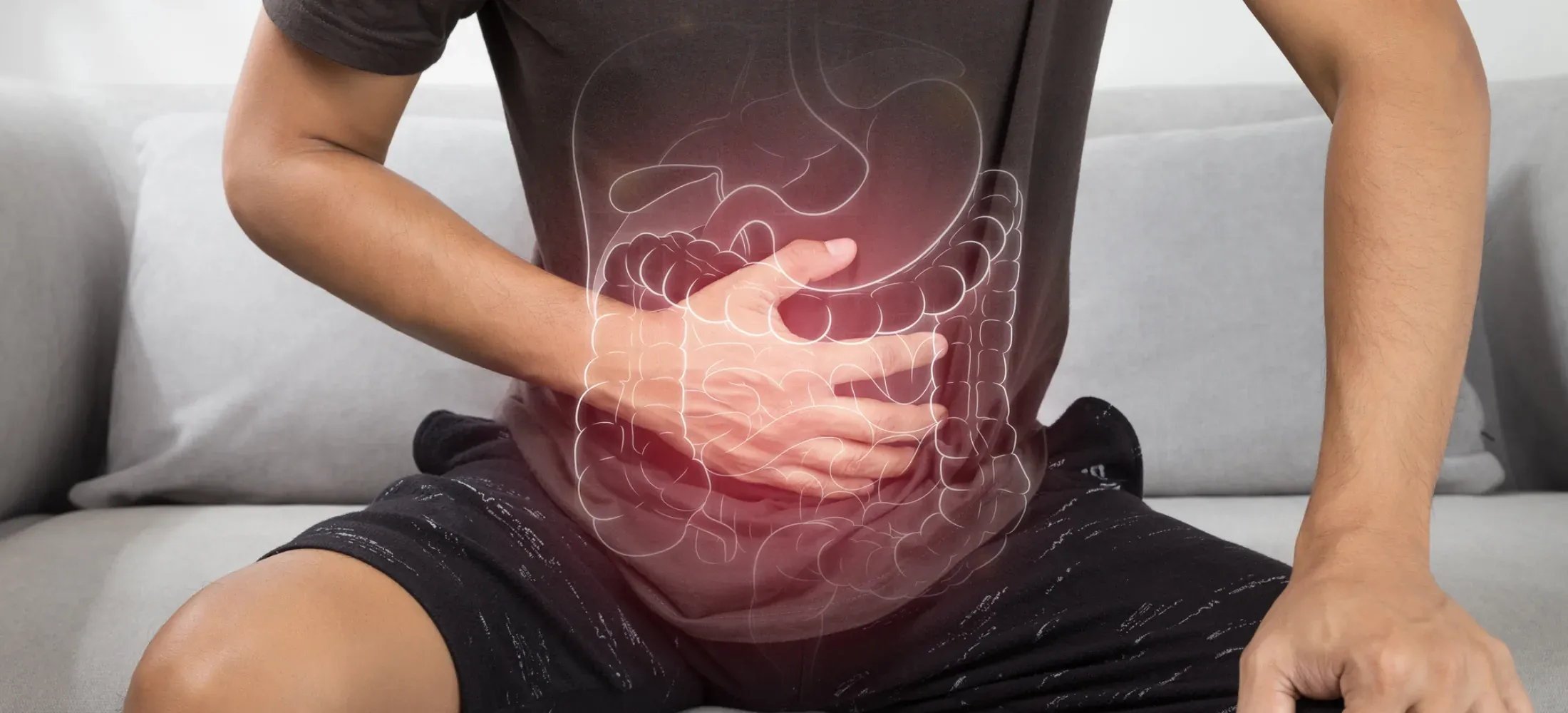A person sitting on a sofa with both hands over their abdomen, the digestive tract drawn over the stomach