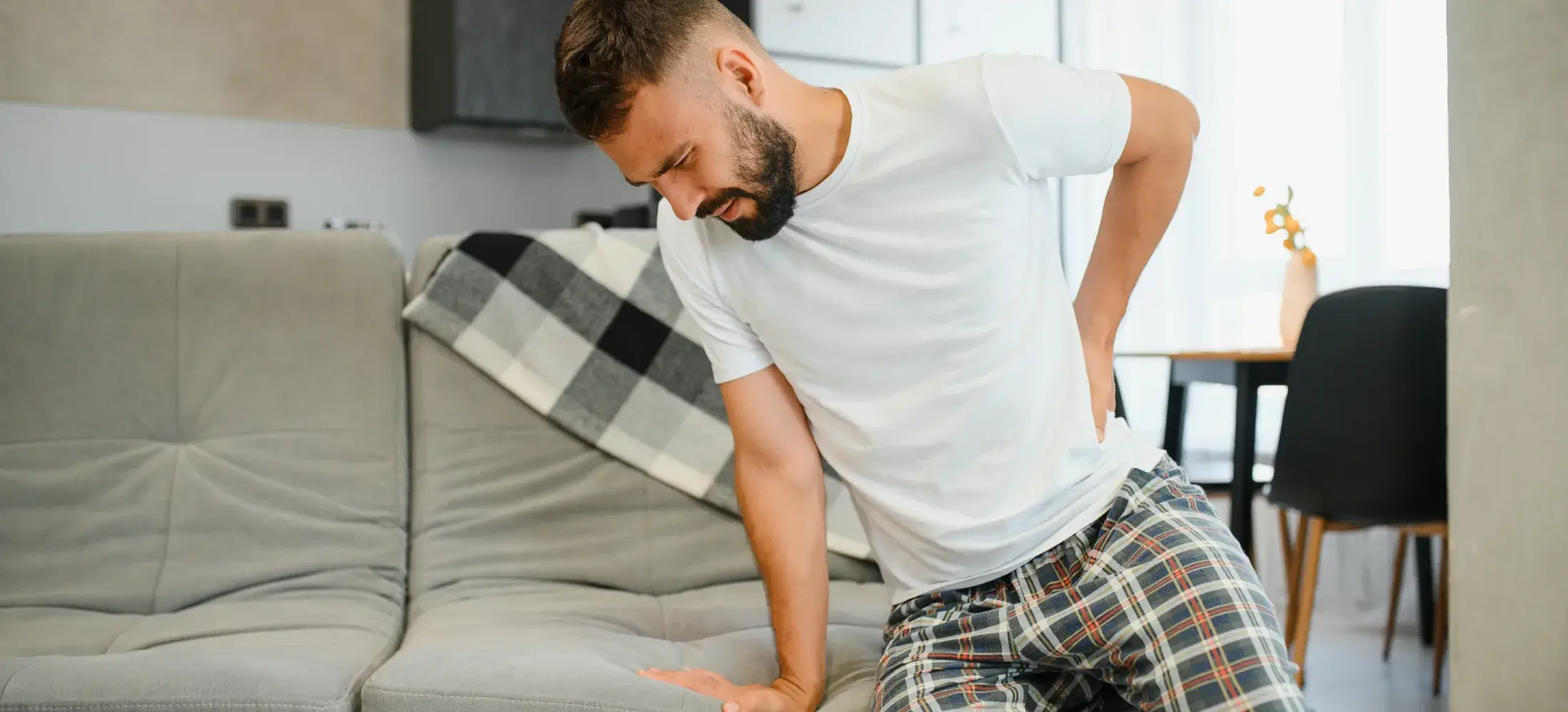 A man pushing up from a sofa with one hand pressed into his lower back