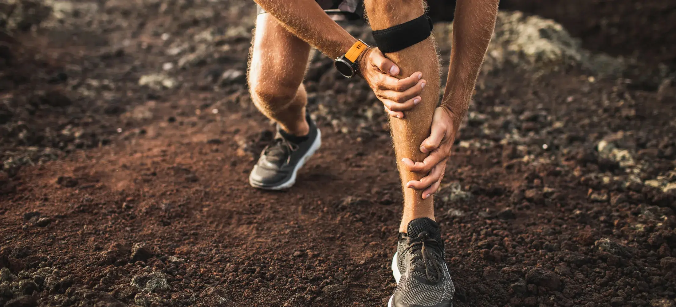 A trail runner stopped on rocky ground, holding the front of a shin