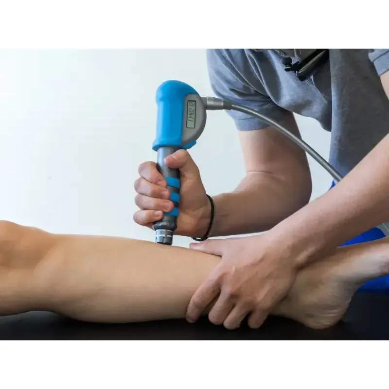 A practitioner applying a shockwave therapy handpiece to a patient's shin