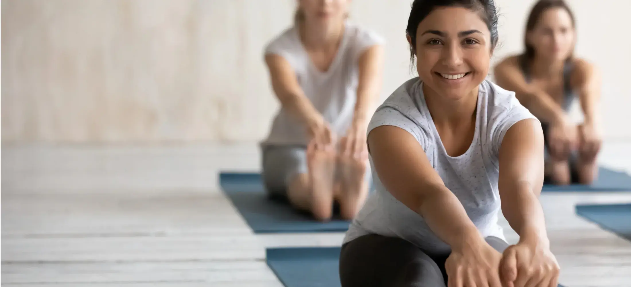 Three people seated on mats in a bright studio, stretching forward towards their toes