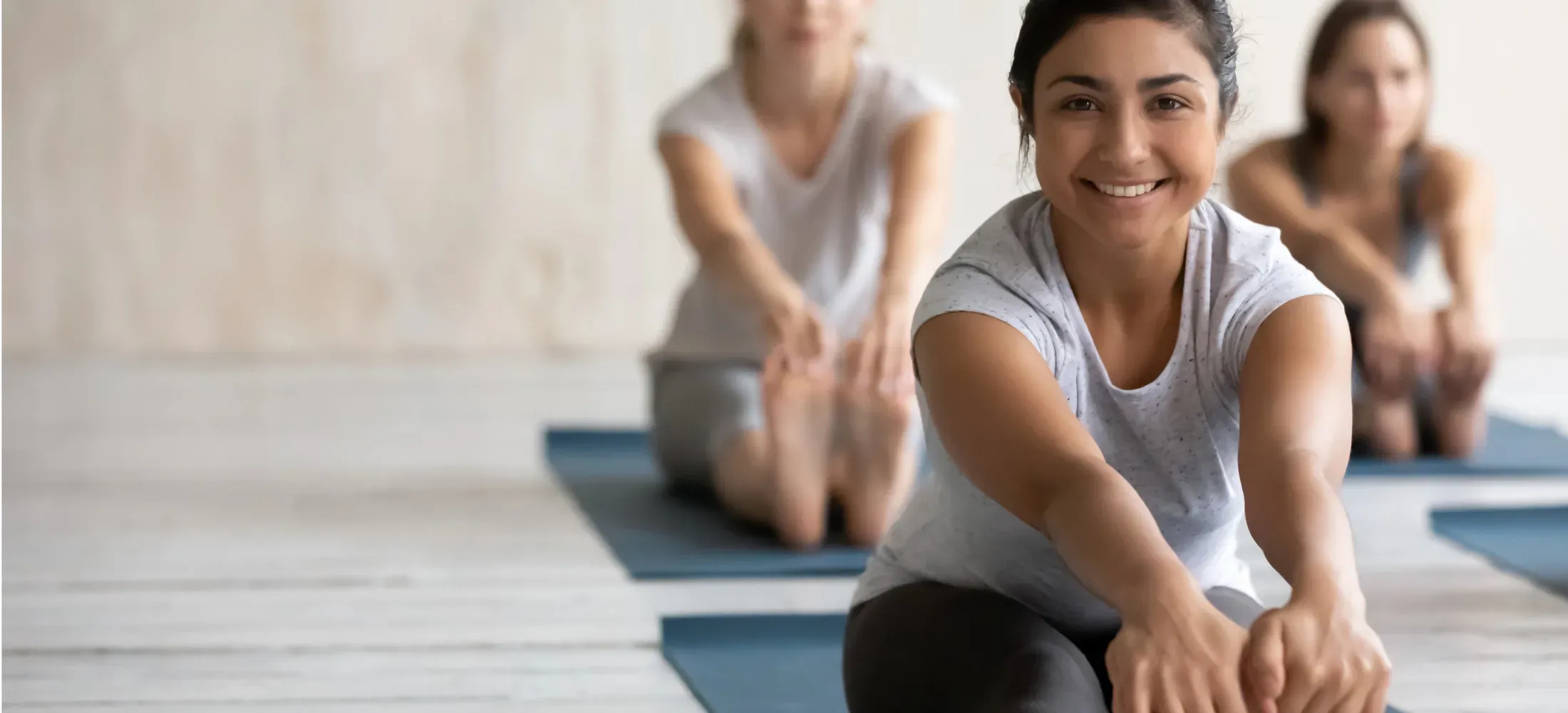 Three people seated on mats in a bright studio, stretching forward towards their toes