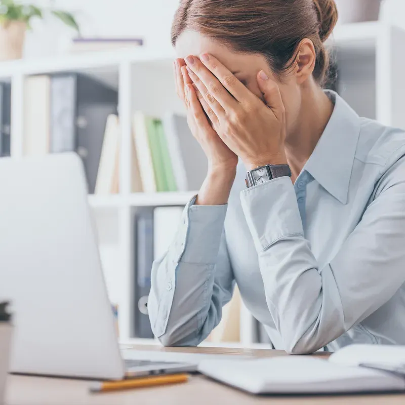 A woman at an office desk with her head in her hands in front of a laptop
