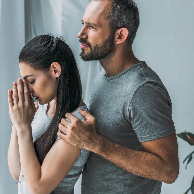 A woman with her head in her hands and a man's hand resting on her shoulder