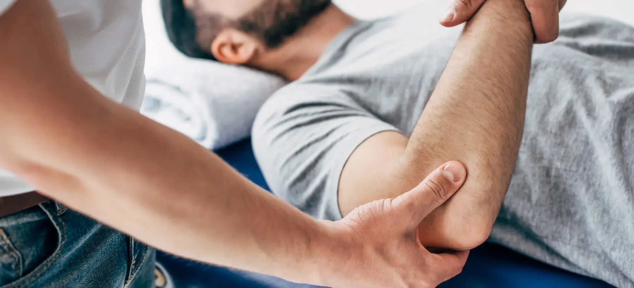 A practitioner examining a patient's elbow while the patient lies on a treatment table