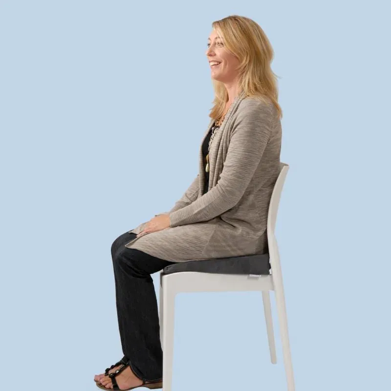 A woman sitting upright on the wedge on a dining chair, the cut-out at the back under her tailbone