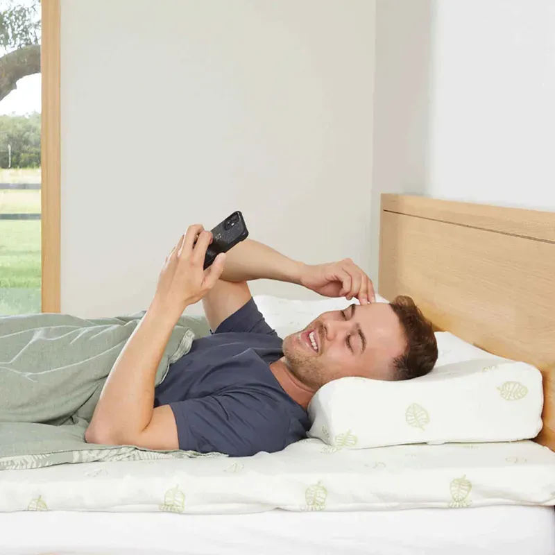 A man lying on his back on the pillow, reading his phone