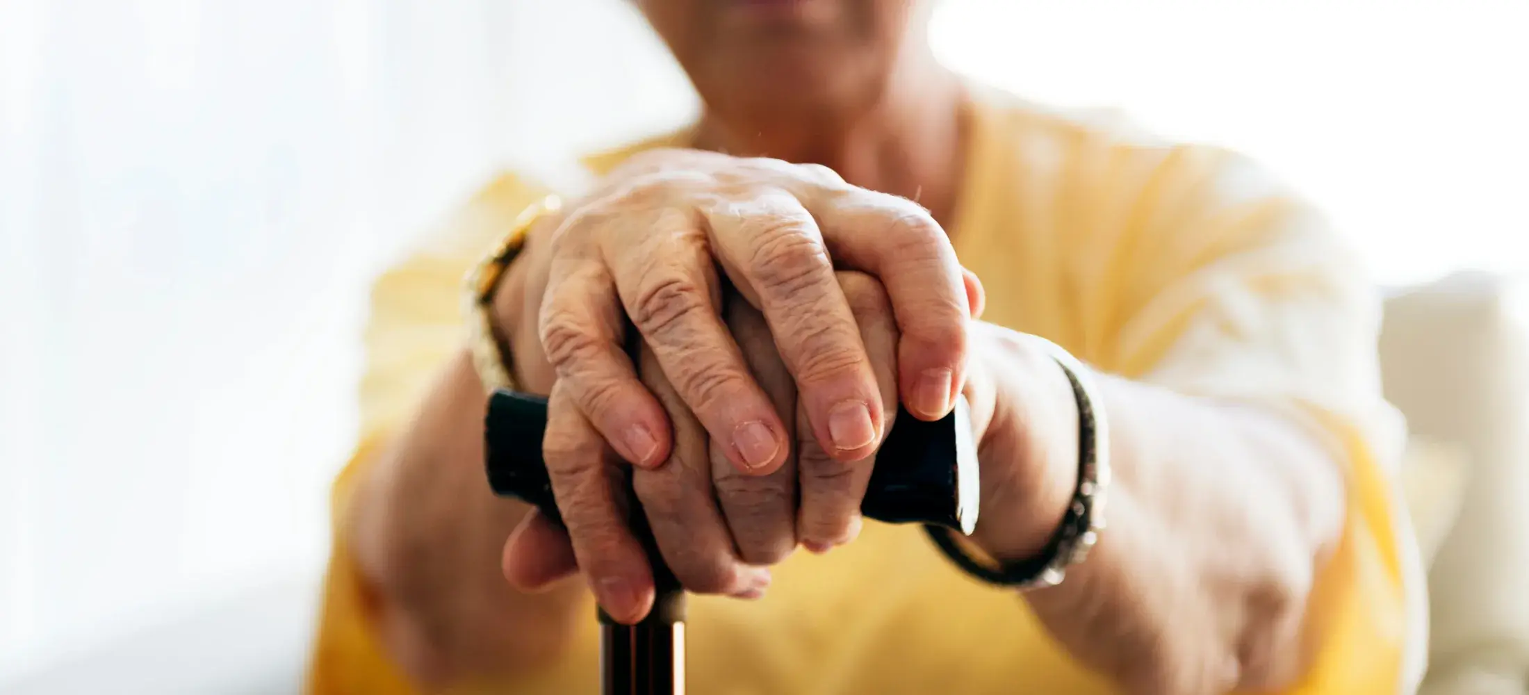 An older person's hands resting on the handle of a walking stick