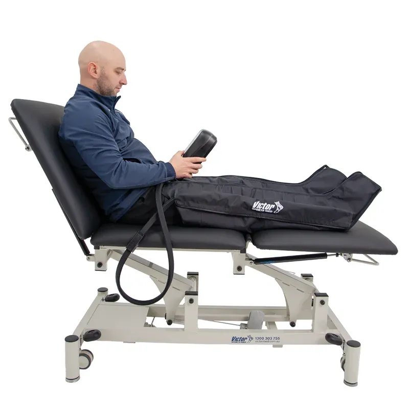 Both boots worn by a man reclining on a treatment table, showing that they reach from foot to upper thigh