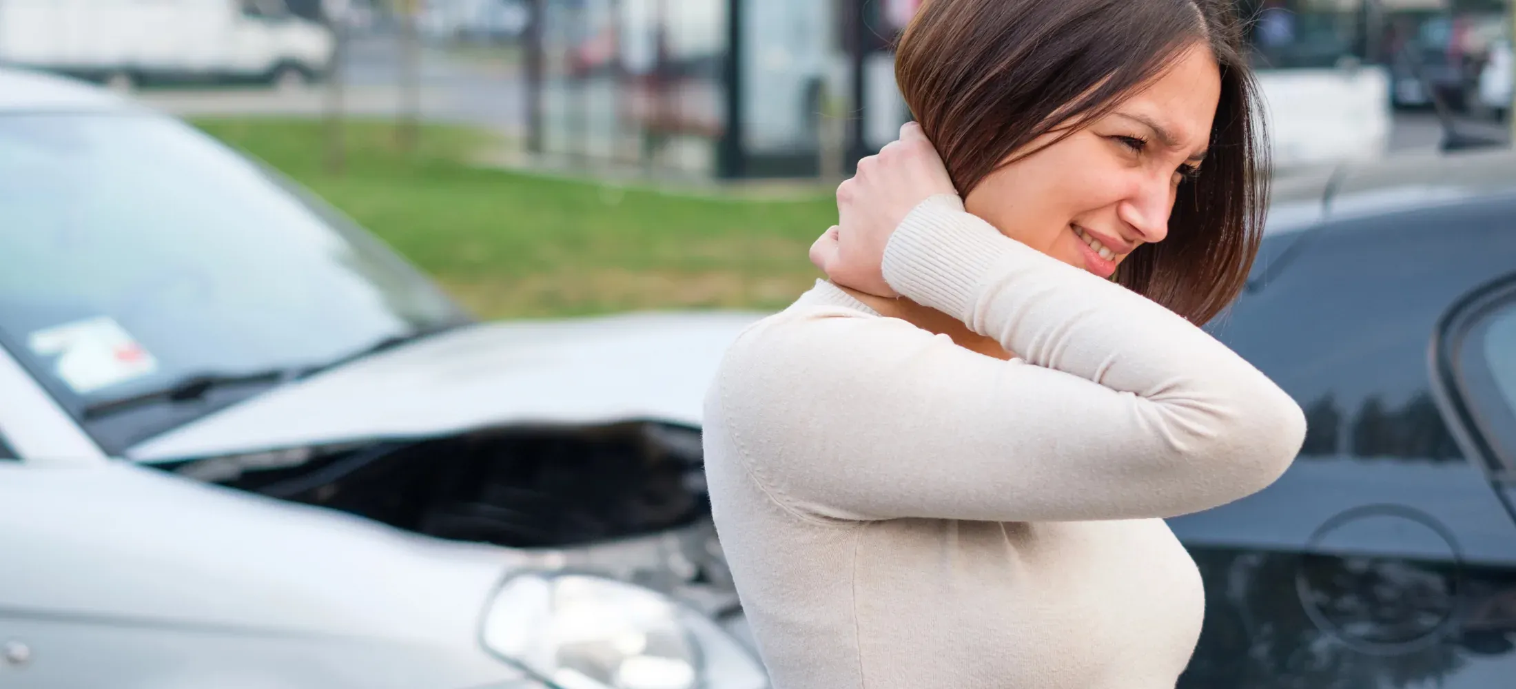A woman holding the back of her neck in front of two cars after a collision