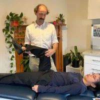 Physiotherapist assessing a patient's leg movement at Brunswick Health clinic.