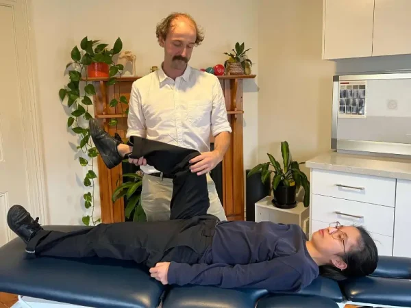 Physiotherapist assessing a patient's leg movement at Brunswick Health clinic.