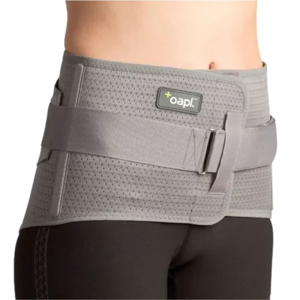 Close-up of a woman wearing a gray sacro-cinch low back support belt, designed for lumbar stabilization and pain relief.