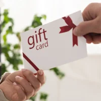 Close-up of hands exchanging a gift card voucher for a massage therapy session.