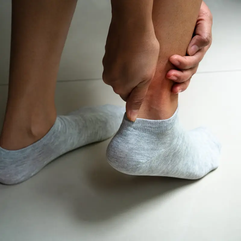 Close-up of a person wearing socks, grasping their right Achilles tendon in pain, indicative of Achilles tendinopathy foot injury