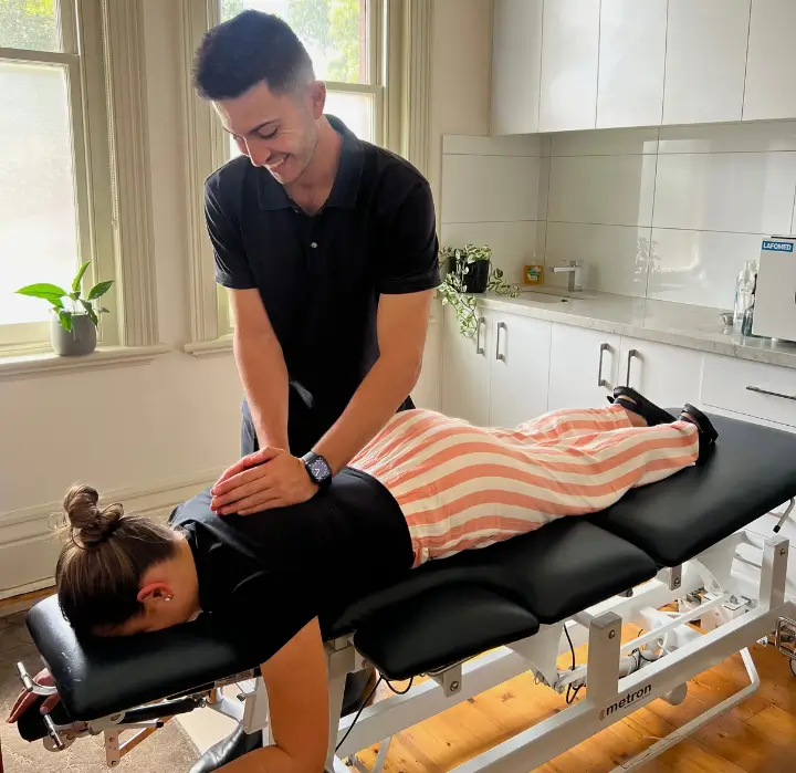 Melbourne Chiropractor performing a mid back adjustment on a patient lying on a treatment table in a well-lit clinic room