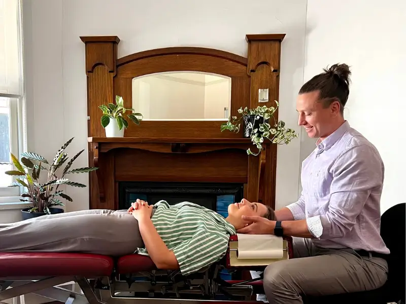 Chiropractor performing a neck adjustment on a patient lying on a treatment table in a well-lit clinic room