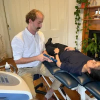 Physiotherapist Andrew Macdonald performing shock wave therapy on a patient's forearm.