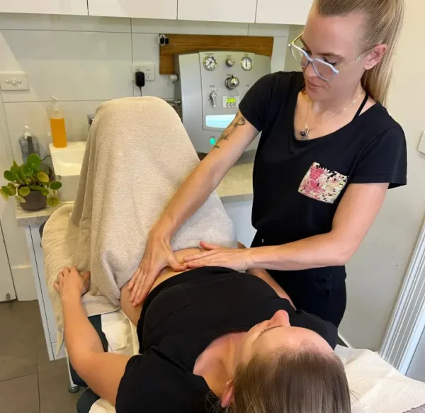 Colonic hydrotherapist performing a colonic irrigation procedure on a patient in a clinic setting.