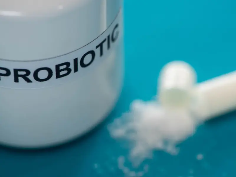 Close-up of a probiotic supplement container and opened capsule with powder spilling out, used for colonic irrigation infusions.