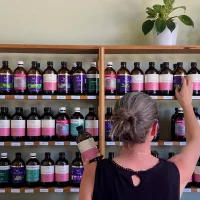 Naturopath Sara Canney selecting a bottle from a shelf full of herbal tinctures at a naturopathy clinic