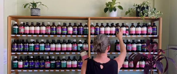 Naturopath Sara Canney selecting a bottle from a shelf full of herbal tinctures at a naturopathy clinic