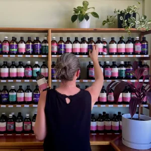 Naturopath Sara Canney selecting a bottle from a shelf full of herbal tinctures at a naturopathy clinic