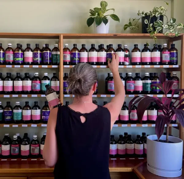 Naturopath Sara Canney selecting a bottle from a shelf full of herbal tinctures at a naturopathy clinic