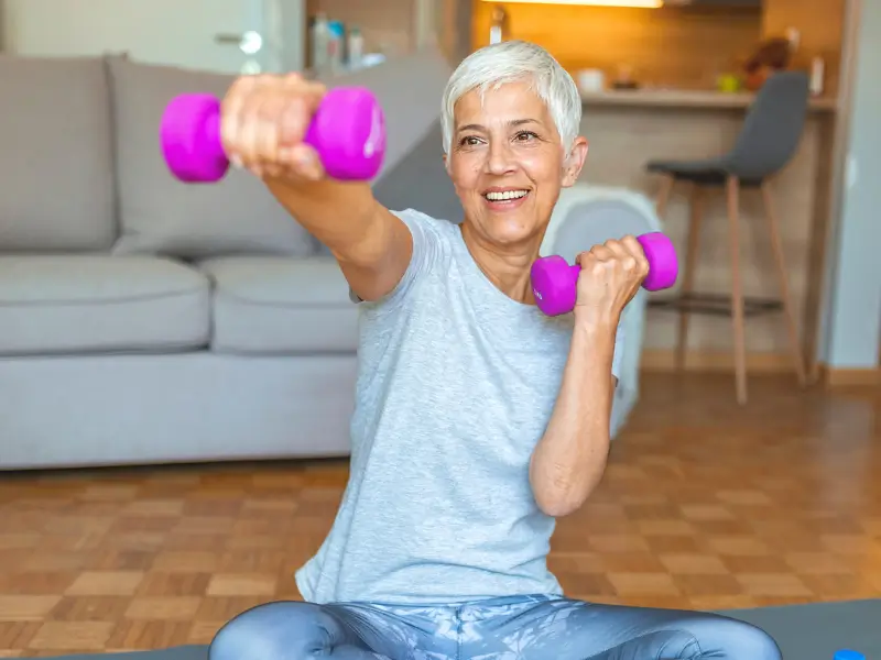 Elderly woman exercising with dumbbells, demonstrating osteoporosis rehabilitation treatment.