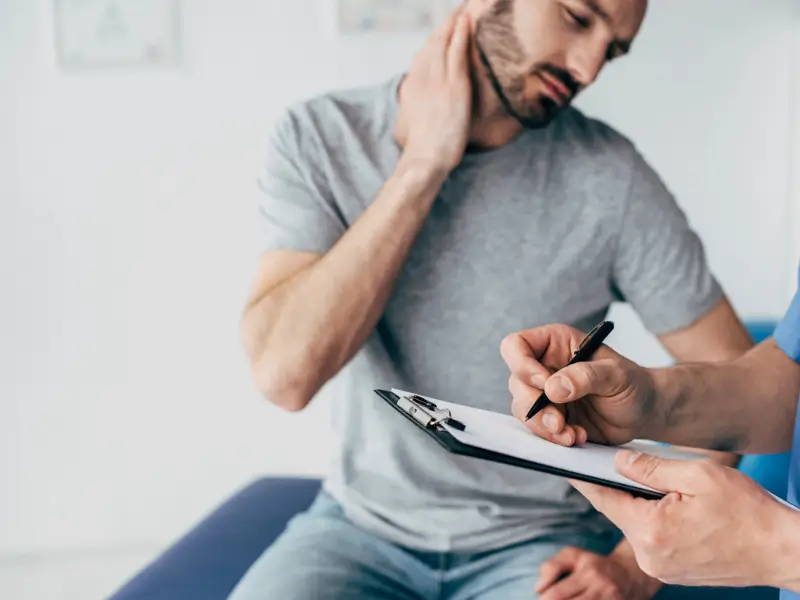 Patient consulting with a physiotherapist about neck pain, while the physiotherapist takes notes on a clipboard