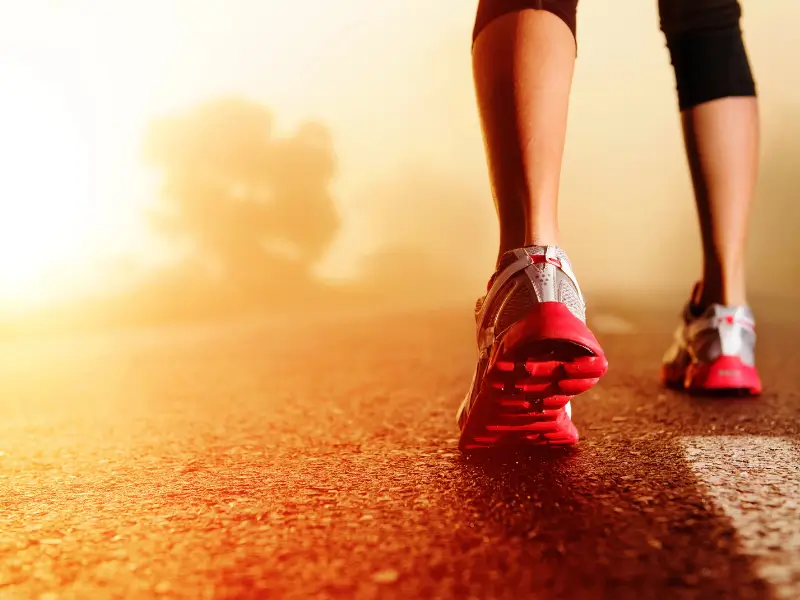 Close-up of a physiotherapist running on a path at sunrise, wearing red and white running shoes.