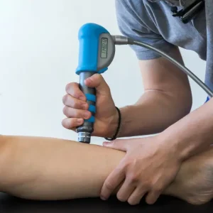 Physiotherapist or chiropractor performing shockwave therapy on a patient's shin to treat shin pain.