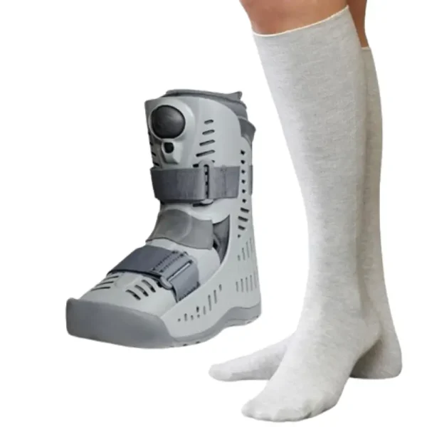 Close-up of a person's lower leg fitted with a modern gray walker boot for foot and ankle stabilization, worn over a white seamless sock.