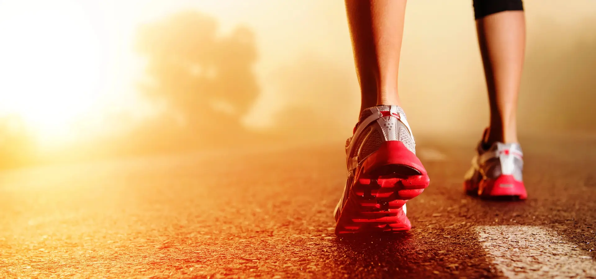 Close-up of a physiotherapist running on a path at sunrise, wearing red and white running shoes.