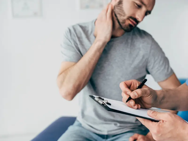 Patient consulting with a physiotherapist about neck pain, while the physiotherapist takes notes on a clipboard